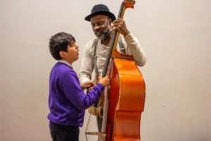 Photo of young audience members exploring a double bass with character Buddy in Rain Rain