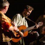 Photo of Bamboozle's PMLD production Makara and the Mountain Dragon. The character Dimitar plays the acoustic guitar up close for an audience member.