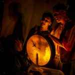 Photo of Bamboozle's PMLD production Makara and the Mountain Dragon. A light shines behind the skin of a drum, illuminating shadow puppets of a dragon flying.