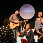 Photo of Bamboozle's AS production Moon Song. Four performances sing the Hello song to individual audience members, accompanied by live guitar music.