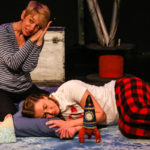 Photo of Bamboozle's AS production Moon Song. One actor falls sleep with her toy rockets. One actor next to her tells the audience her story.