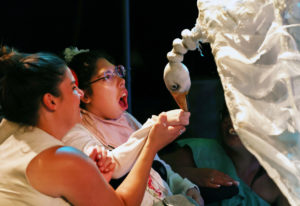 Photo of one of our participants reaching out to a large puppet of a white goose whose head inclines towards their outstretched hand.