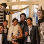 Photo of gala guests dressed in black and white, having their photo taken with stilt walkers