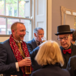 Photo of Gala guests wearing top hat and scarf, enjoying a drink at the event
