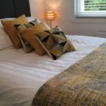 Photo showing a comfortable double bed with white bed linen and yellow and grey scatter cushions