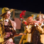 The images show Patience approaching her friend Bird with a handful of cornflakes. Patience wears a straw hat and a peach coloured floral dress. Bird is a puppet resembling a chicken made of our recycled cogs with a plume of red feathers on his head.