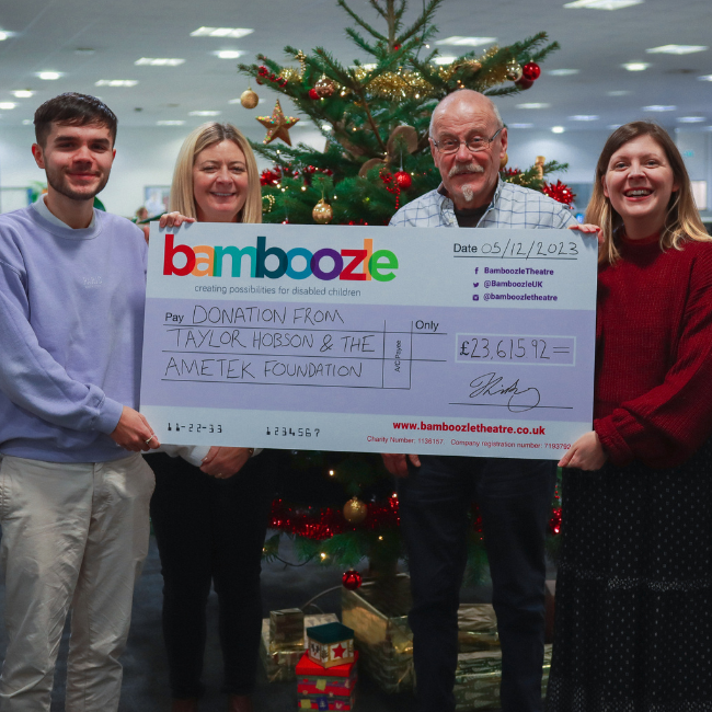 Photo showing Taylor Hobson and Bamboozle staff holding a large cheque in front of a Christmas tree.