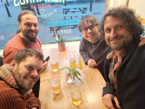 Lou on tour with David, Tim and Ben. They are taking a selfie whilst having a drink in a pub.
